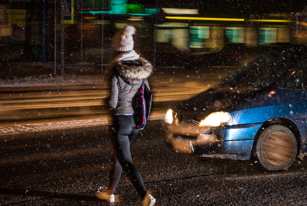 Person crossing street at night in front of an oncoming car. Daylight Saving Time and drowsy driving awareness plus safety tips.